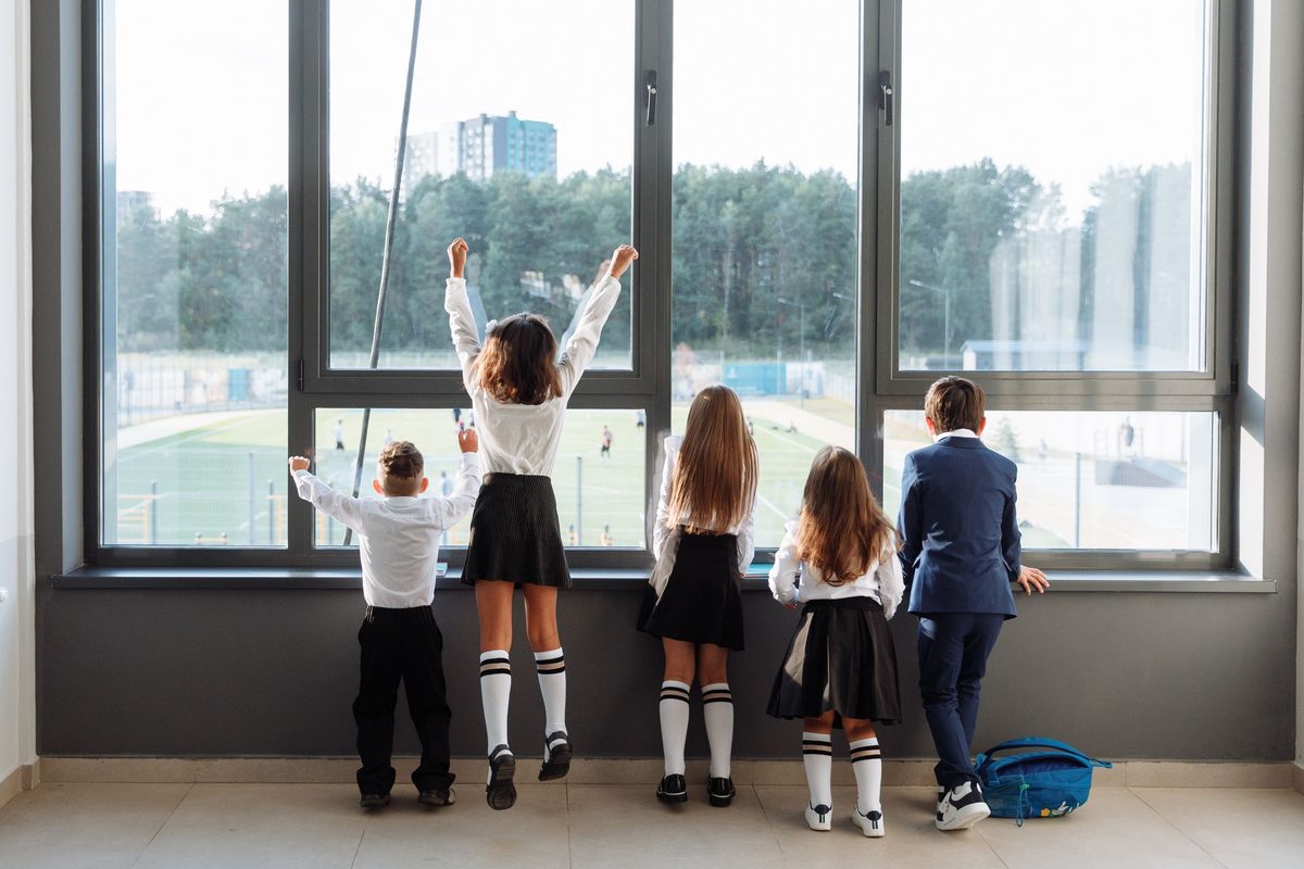 Alumnos de espaldas con el uniforme del colegio mirando por una ventana
