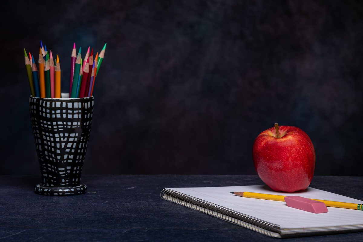 Lápices de colores, un cuaderno y una manzana sobre un pizarrón